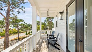 A covered porch with a railing, two Adirondack chairs, and a door with a glass panel. - Modern Pet-Friendly Retreat for Families w/2 Bunk Rooms | Brand New Pool! (Seagrove Beach)