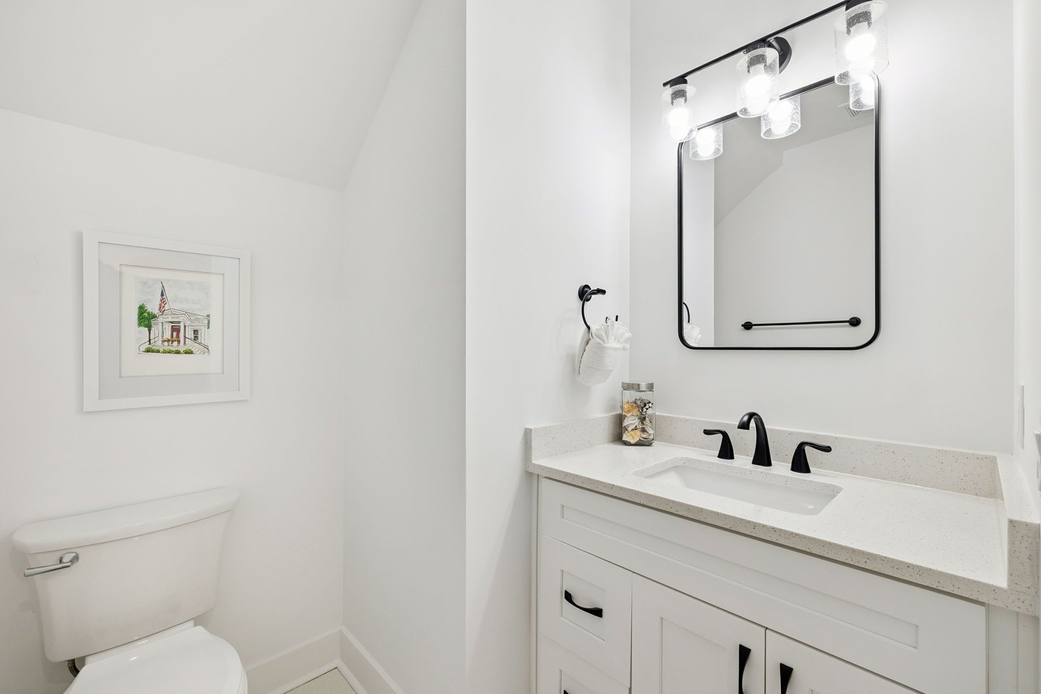 A bathroom with a white toilet, a sink with a mirror above it, and a framed picture on the wall.