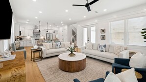 A spacious living area with a round coffee table, sofas, and a kitchen in the background. - Modern Pet-Friendly Retreat for Families w/2 Bunk Rooms | Brand New Pool! (Seagrove Beach)