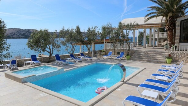A pool area with two pools, lounge chairs, and a view of the sea. - Adriatic Apartment With Large Terrace (Novalja)