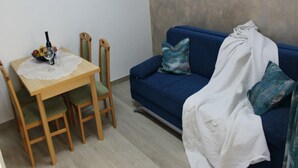 A small living area with a dining table, chairs, a blue sofa with a white blanket, and a wall with a textured finish. - Adriatic Apartment With Large Terrace (Novalja)
