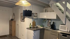 Una cucina compatta con frigorifero, microonde e lavello. C'è un piccolo tavolo da pranzo con una sedia e una scala che conduce a un livello superiore.