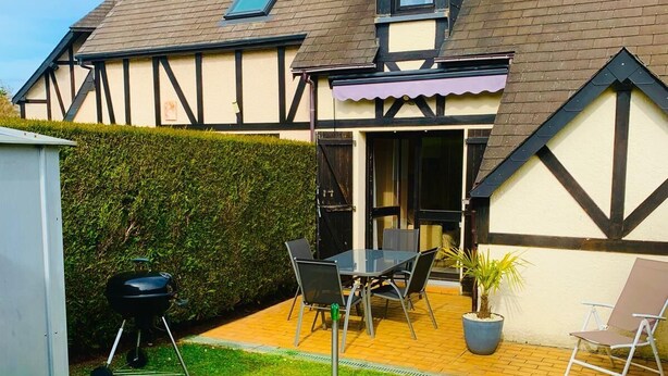 Una casa con un patio attrezzato con tavolo e sedie, un barbecue e una poltrona da relax.