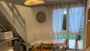 Una stanza accogliente con un tavolo da pranzo in legno, sedie, un divano, un forno a microonde e una sveglia appesa al muro.