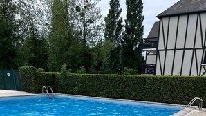 Una piscina con bordo piastrellato, circondata da siepi e alberi.