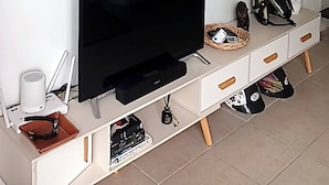 Ein modernes Wohnzimmer mit einem großen abstrakten Gemälde an der Wand, einem Flachbildfernseher, einer weißen Unterhaltungsanlage mit Schubladen und einem Blumentopf.