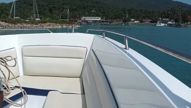 Ein Boot mit weißem Interieur und Blick auf eine Marina mit Booten und Gebäuden im Hintergrund.