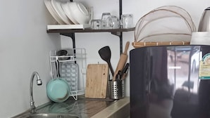 Eine Küche mit Spüle, einem schwarzen Kühlschrank und einem Regal mit Geschirr und Gewürzen.