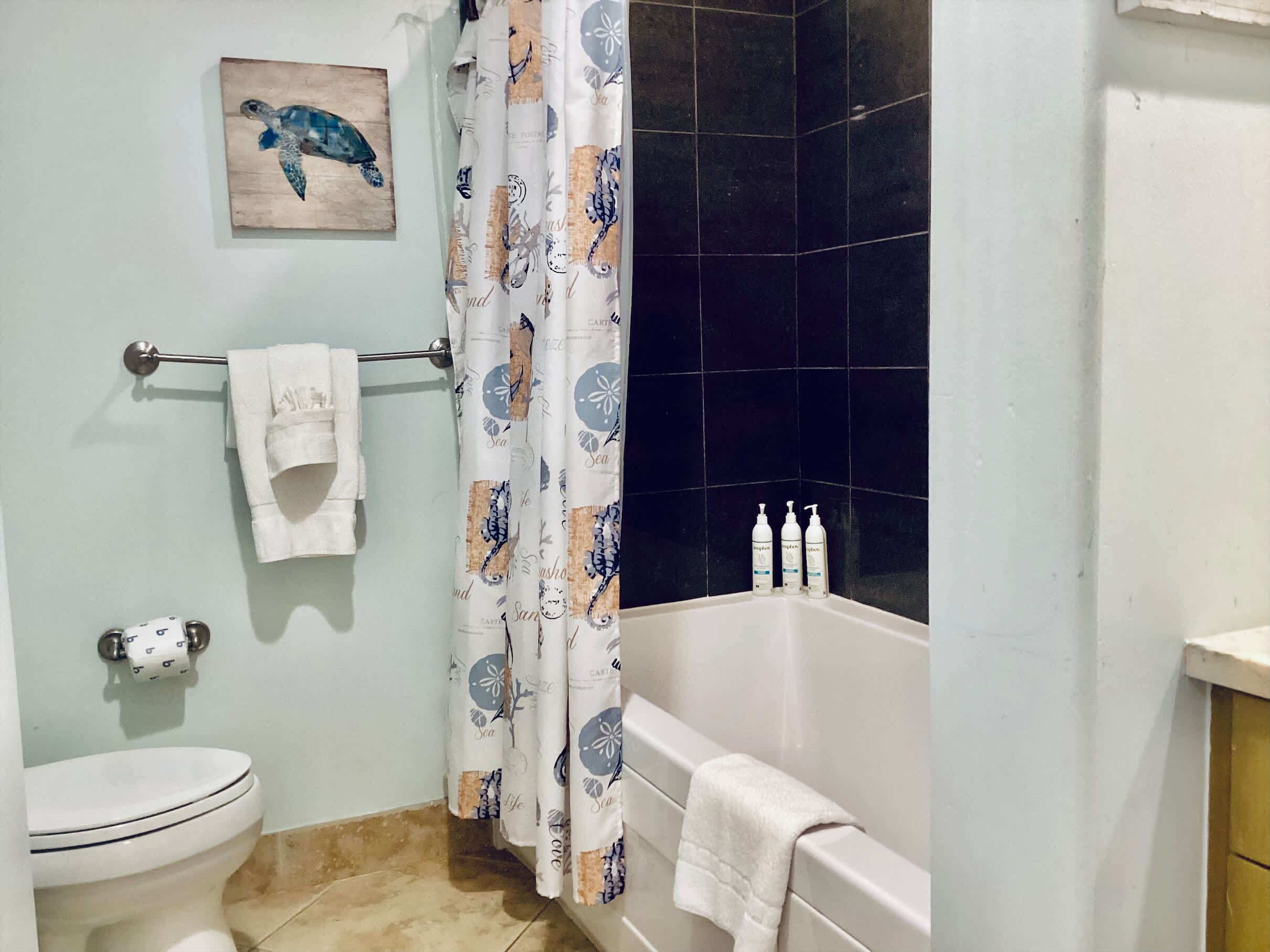 A bathroom with a toilet, a bathtub, a shower curtain with sea turtle designs, and a towel rack with a towel.