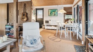 Ett mysigt vardagsrum med ett träpanelat tak, en vit soffa, ett matbord med stolar och en gitarr på väggen.