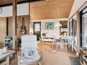 Ein gemütliches Wohnzimmer mit Holzbalkendecke, einer weißen Couch, einem Esstisch mit Stühlen und einer Gitarre an der Wand.