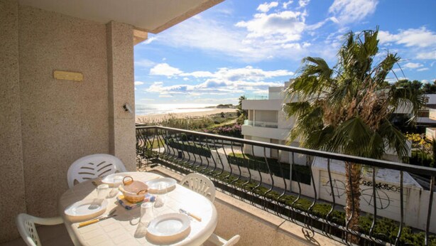 Varanda com mesa posta para refeições, vista para uma praia e palmeiras.