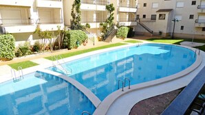 Uma piscina com borda curva, rodeada por um gramado bem cuidado e um edifício com varandas.