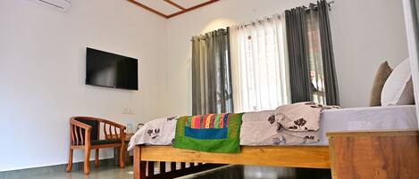 A room with a bed, a chair, a TV, and a window with curtains.