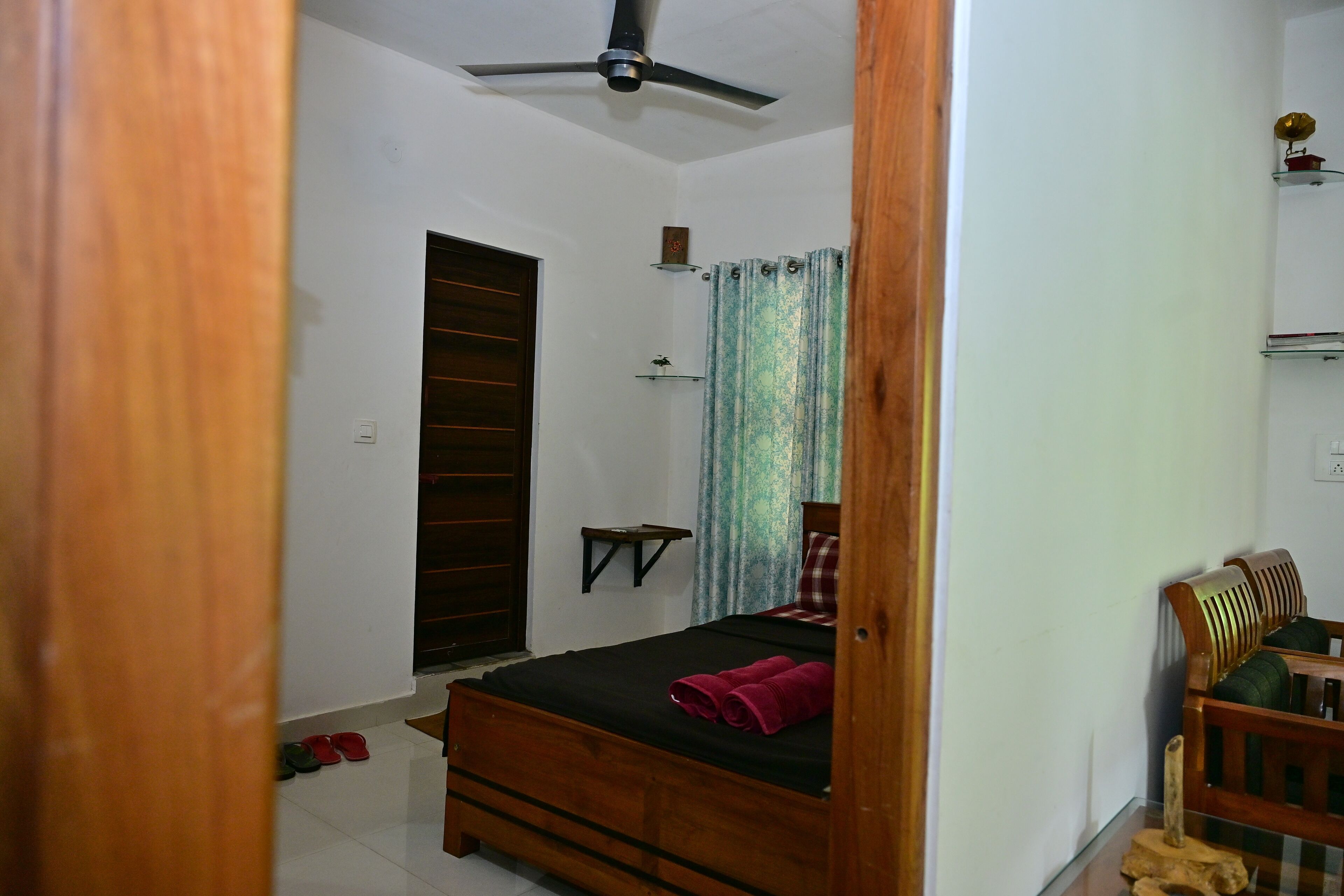 A bedroom with a bed, a ceiling fan, a wardrobe, a shelf, and a chair.