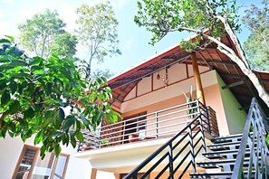 A multi-story building with a balcony, stairs, and a tree in the foreground. - 4 Nature stay (Somvarpet)