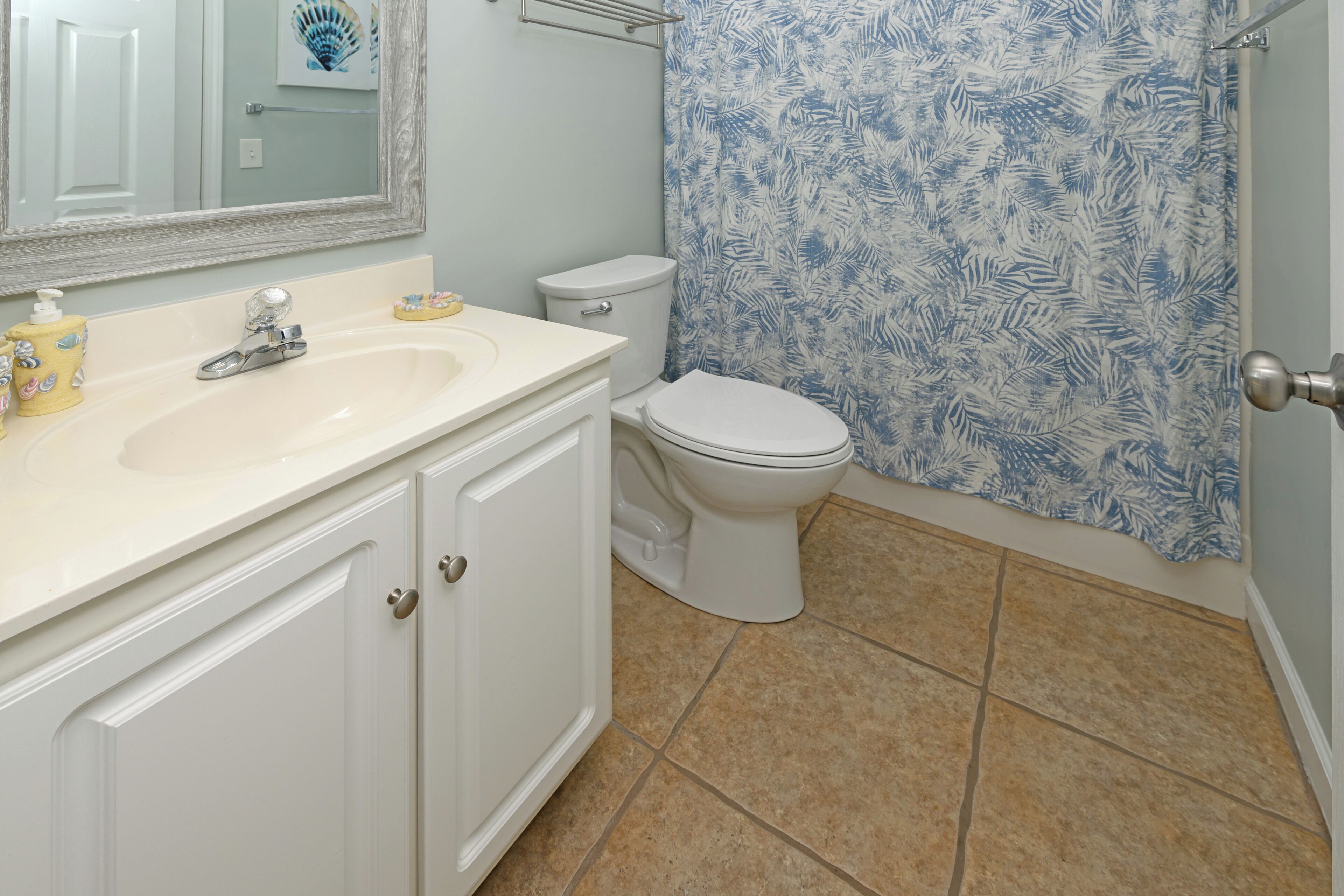 Une salle de bain avec un lavabo blanc, des toilettes et un rideau de douche orné d’un motif de feuilles.