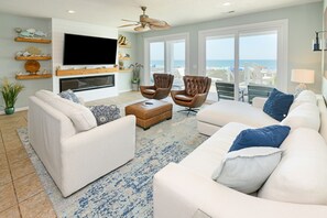 A living room with a fireplace, white sofas, a coffee table, and a TV mounted on the wall. - Oceanfront 5 Bedroom House Next To the Surfside Beach Pier! - Pier Pleasure (Surfside Beach)