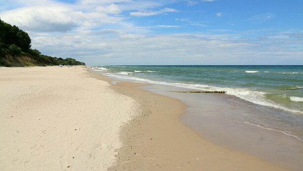 Ein breiter Sandstrand mit sanften Wellen und blauem Himmel.