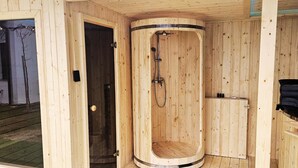 Eine Holzsauna mit gebogener Form, einer Duschbrause und einer kleinen Ablage mit Flaschen.