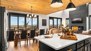 Una cocina amplia con una isla grande, techo de madera y ventanas grandes que ofrecen vistas del paisaje.
