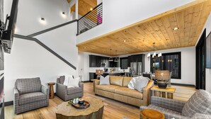 Amplia sala de estar con techo alto, muebles modernos y una cocina al fondo.
