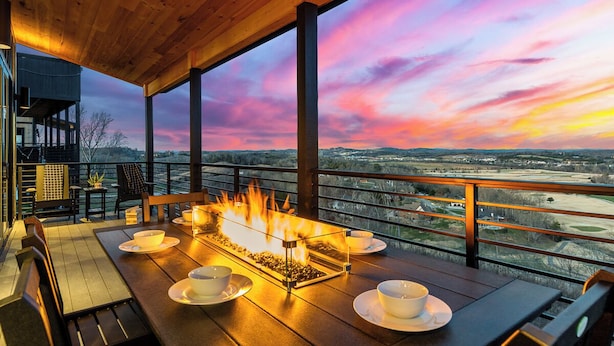 Una terraza de madera con una chimenea, mesa de comedor, sillas y vistas del paisaje.