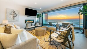A modern living room with a large window overlooking the ocean, a fireplace, and comfortable seating. - Featured on HGTV "Christina On The Coast" - Stunning Ocean Views, Spa! (San Diego)