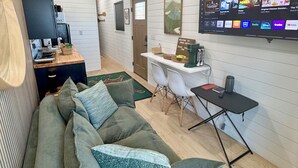 A modern living room with a sofa, a TV mounted on the wall, and a ceiling fan. - Modern and eclectic shipping container home (Whitwell)