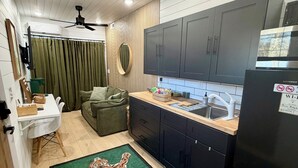 A compact kitchen with dark cabinets, a black refrigerator, and a wooden countertop. - Modern and eclectic shipping container home (Whitwell)