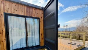 A wooden cabin with a sliding glass door, a deck, and a view of a snowy landscape. - Modern and eclectic shipping container home (Whitwell)