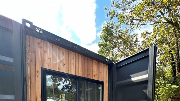 A modern building with a wooden exterior and large glass doors. - Modern and eclectic shipping container home (Whitwell)