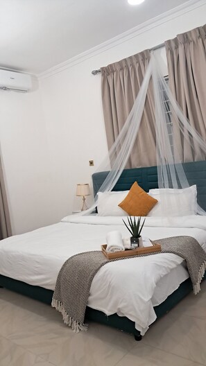 A neatly made bed with white linens, a teal headboard, and a canopy. - Kwaba Villa (Tema)