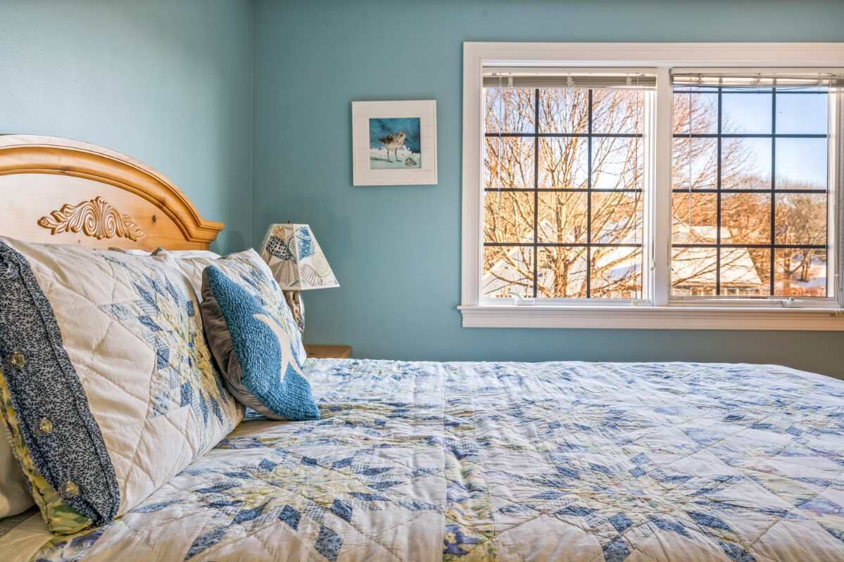 A bedroom with a large bed, a window with a view of trees, and a framed picture on the wall.