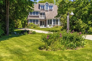 A two-story house with a front porch, a lawn, and a garden with purple flowers. - Town & Tide Home for 8 (Kennebunkport)