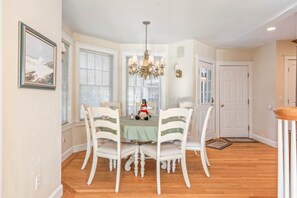 A dining room with a round table, white chairs, a chandelier, and a snowman decoration. - Town & Tide Home for 8 (Kennebunkport)