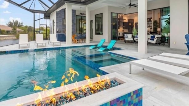 Ein moderner Poolbereich mit Feuerstelle, Liegestühlen und einer überdachten Terrasse.