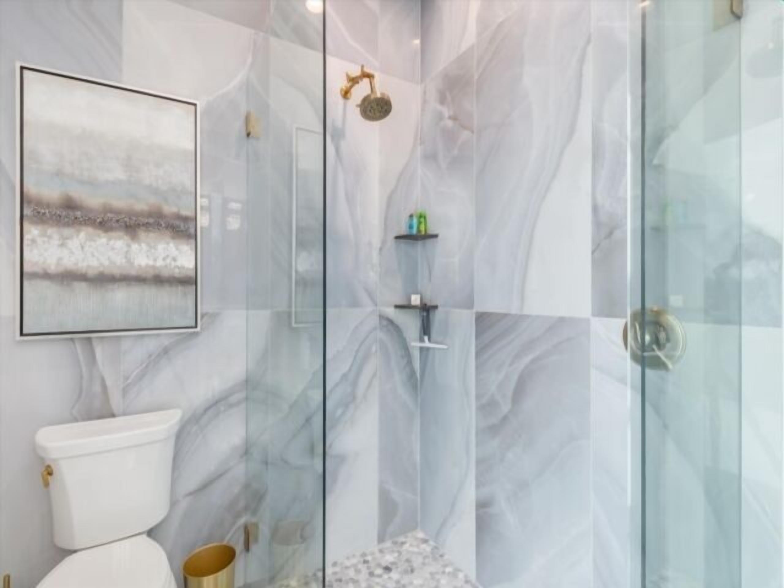 Un bagno con parete in marmo, un water, box doccia in vetro e un quadro appeso alla parete.