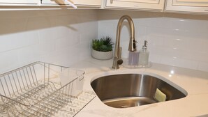 Een keuken met een RVS spoelbak, een draadrek, een potplant en een zeepdispenser.