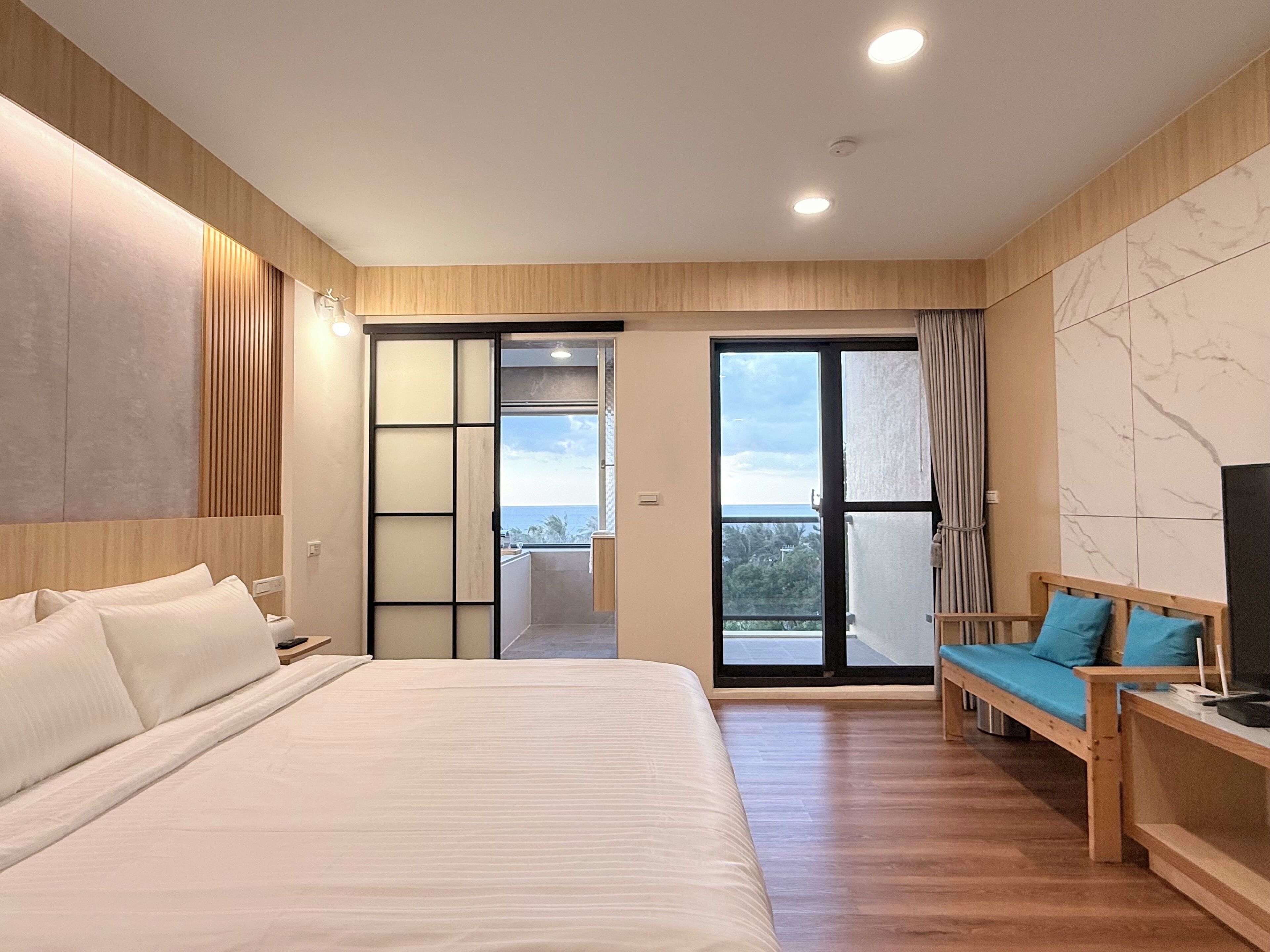 Habitación de hotel moderna con una cama grande, un sofá, un televisor y un balcón con vistas.
