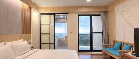 Habitación de hotel moderna con una cama grande, un sofá, un televisor y un balcón con vistas.
