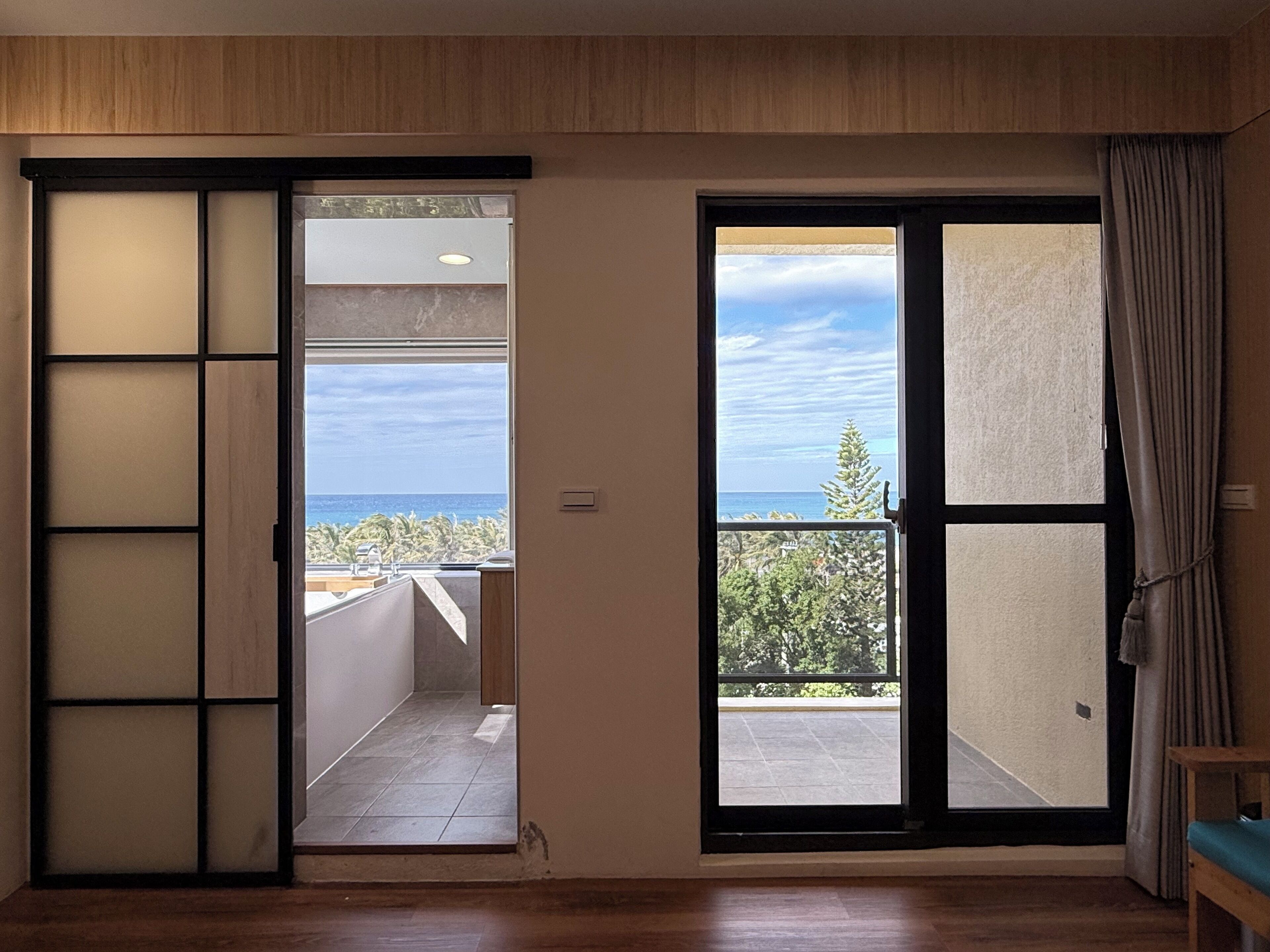 Una habitación con puerta corredera que da a un balcón con vistas al mar y árboles.