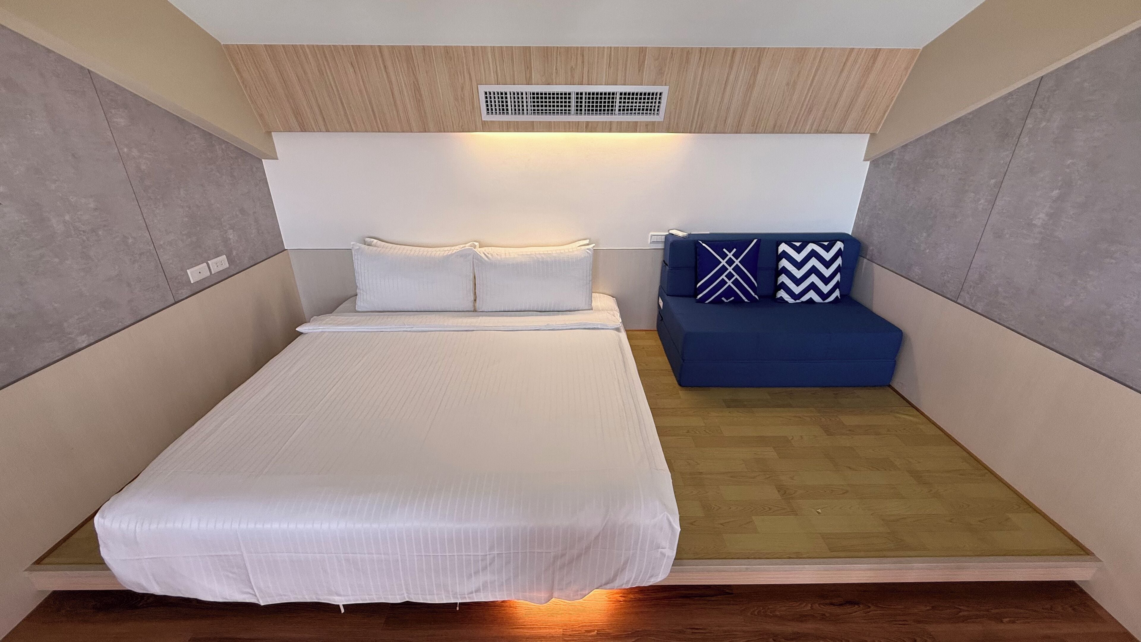 Un dormitorio pequeño con cama, un sofá compacto y un respiradero en el techo.