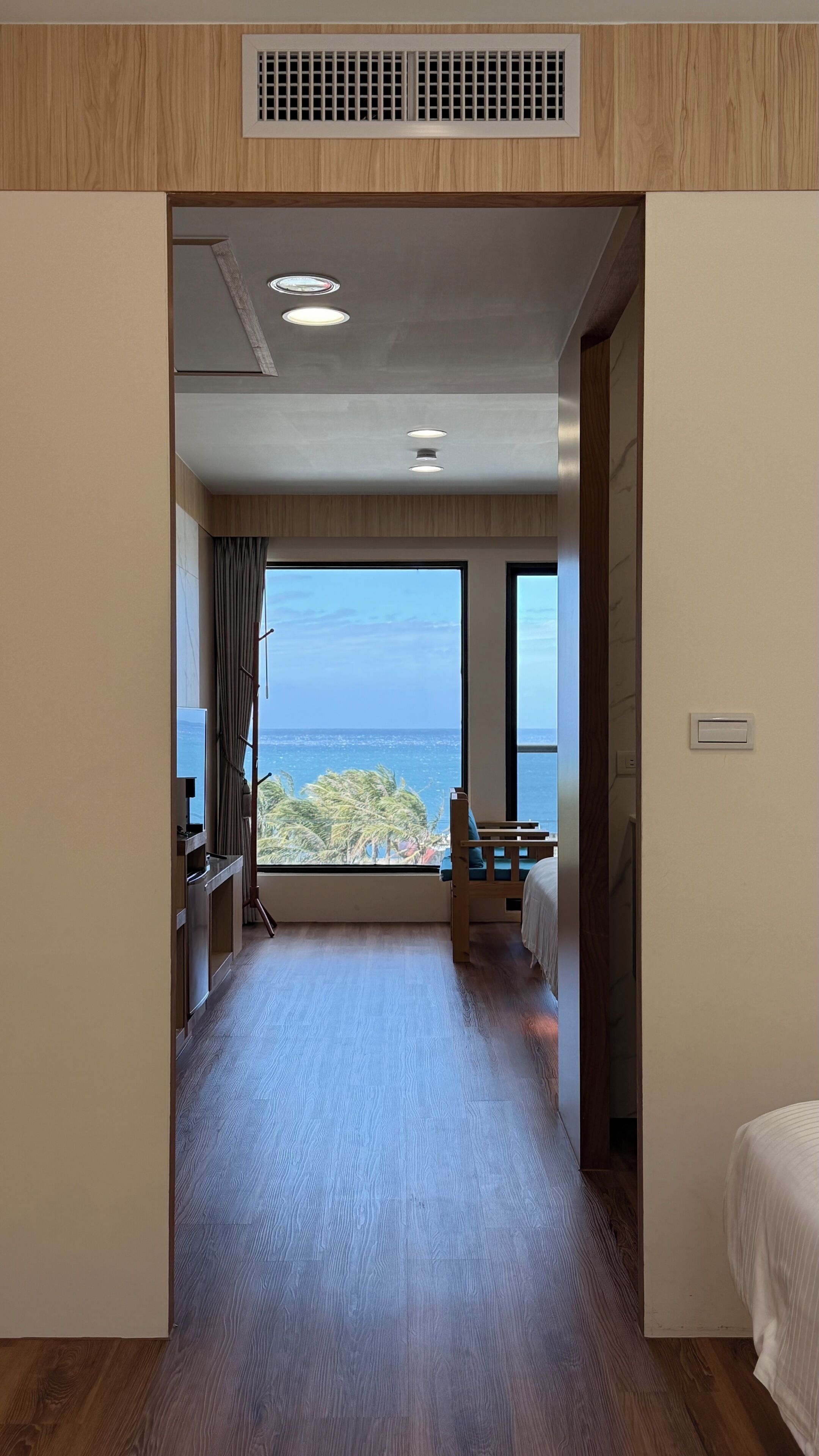A hotel room with a large window offering a view of the ocean, a bed, a desk, and a chair.
