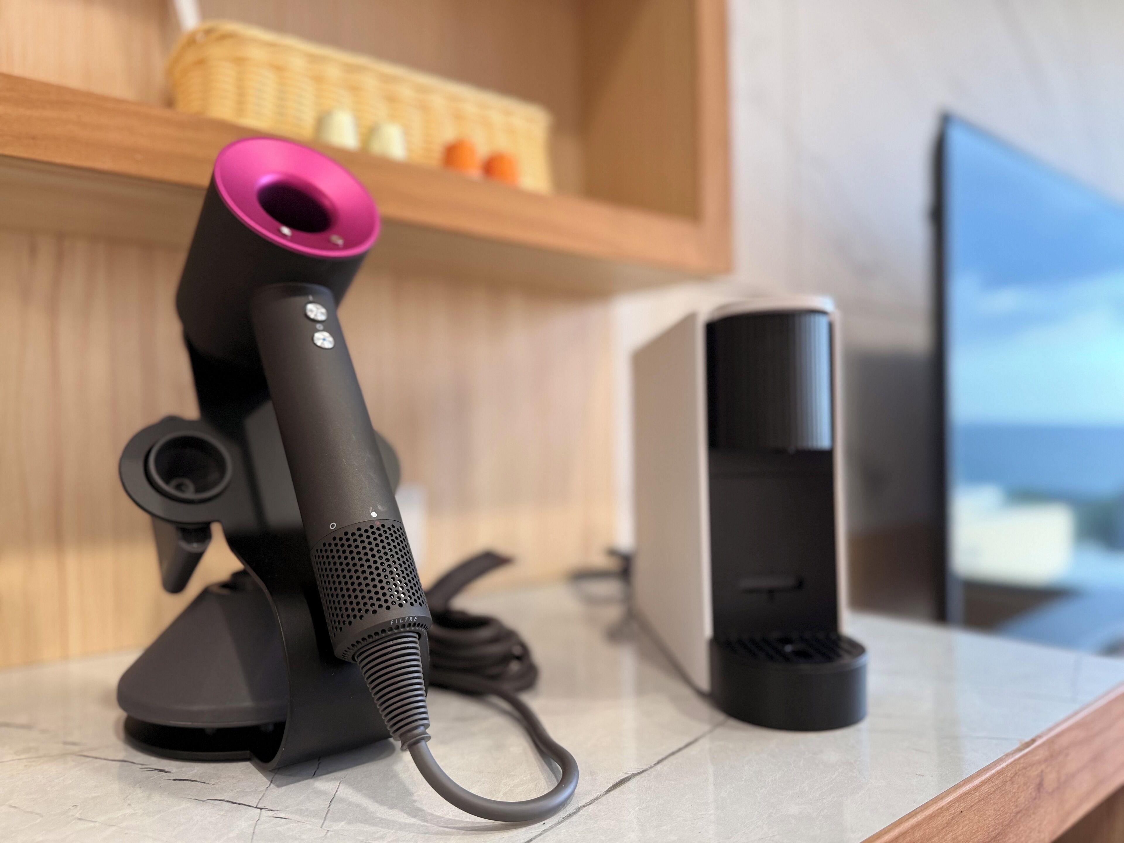A hair dryer with a pink nozzle on a countertop next to a computer.