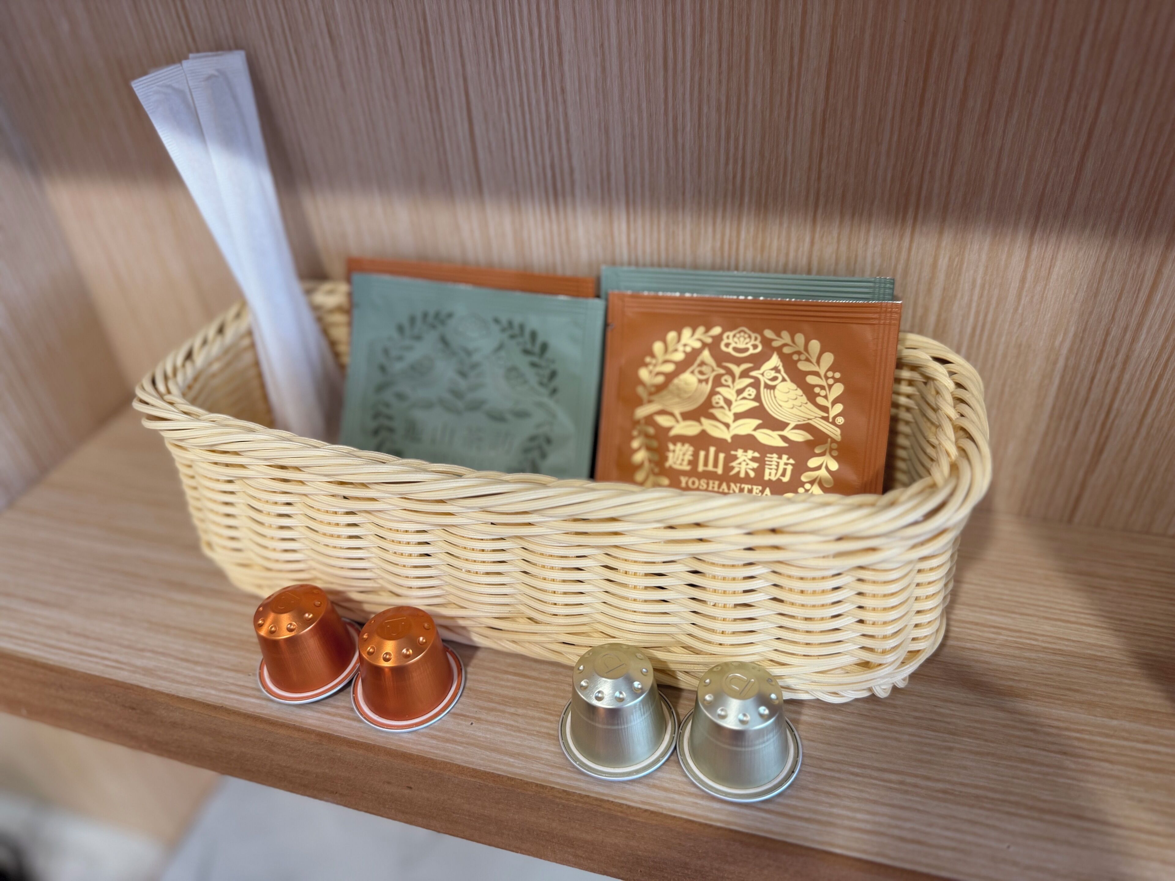 A wicker basket containing tea bags and a book on a wooden shelf.