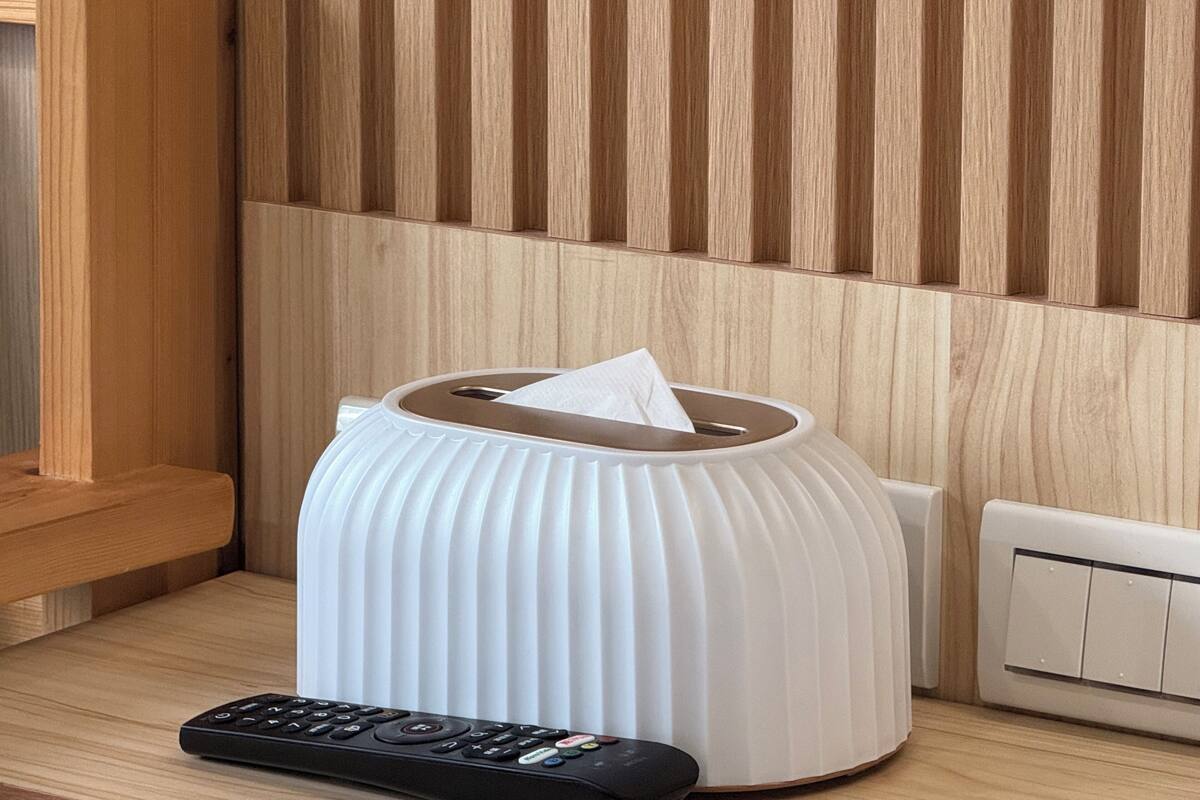 A white tissue box on a wooden table with a remote control beside it.