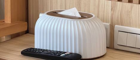 A white tissue box on a wooden table with a remote control beside it.