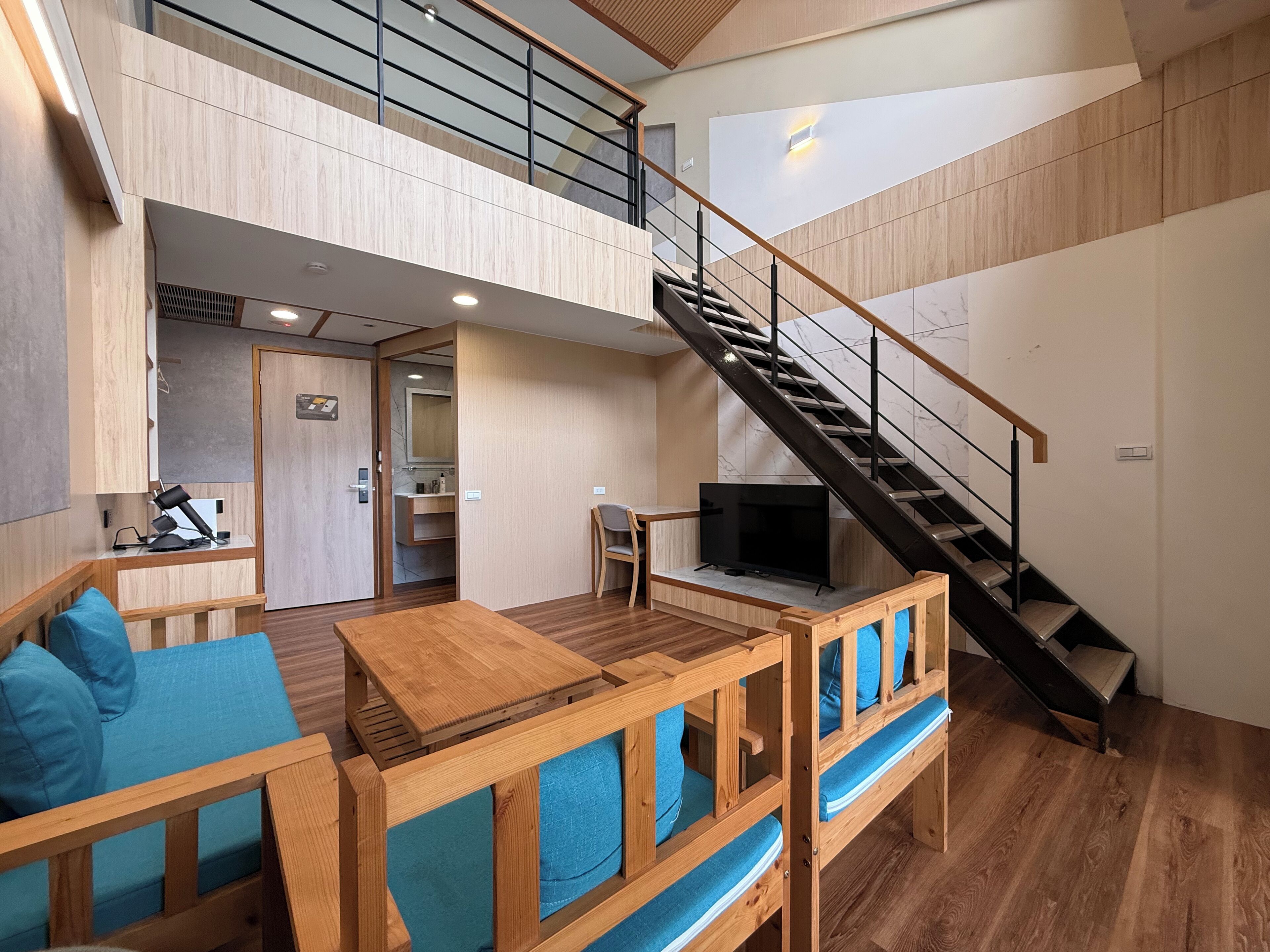 Un vaste espace de vie agrémenté d’un escalier en bois, d’un téléviseur et d’un coin salon avec des coussins bleus.