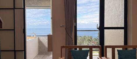 Un balcón con vista al mar, un banco de madera con cojines y una puerta corrediza de vidrio.